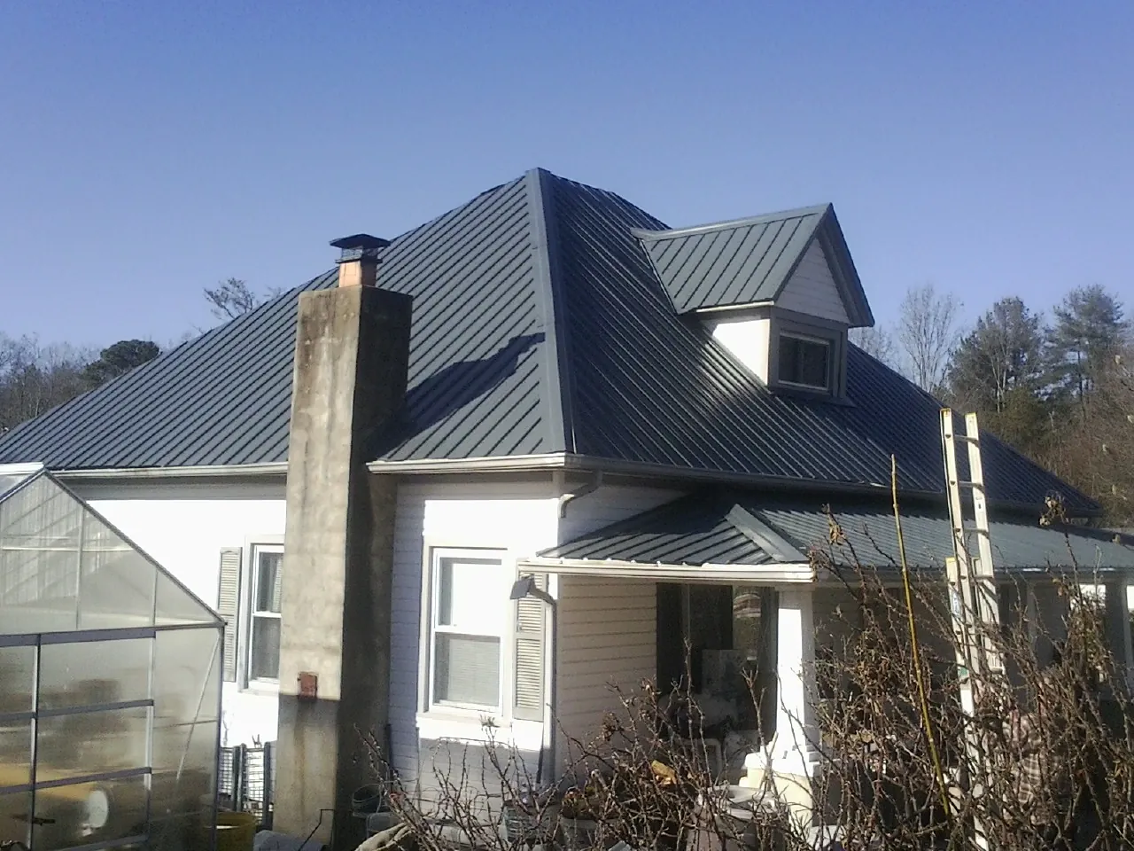 Dark blue standing seam metal roof on a white farmhouse with dormer — Slate & Tile Roof Repair by Roofing Brothers in Braselton