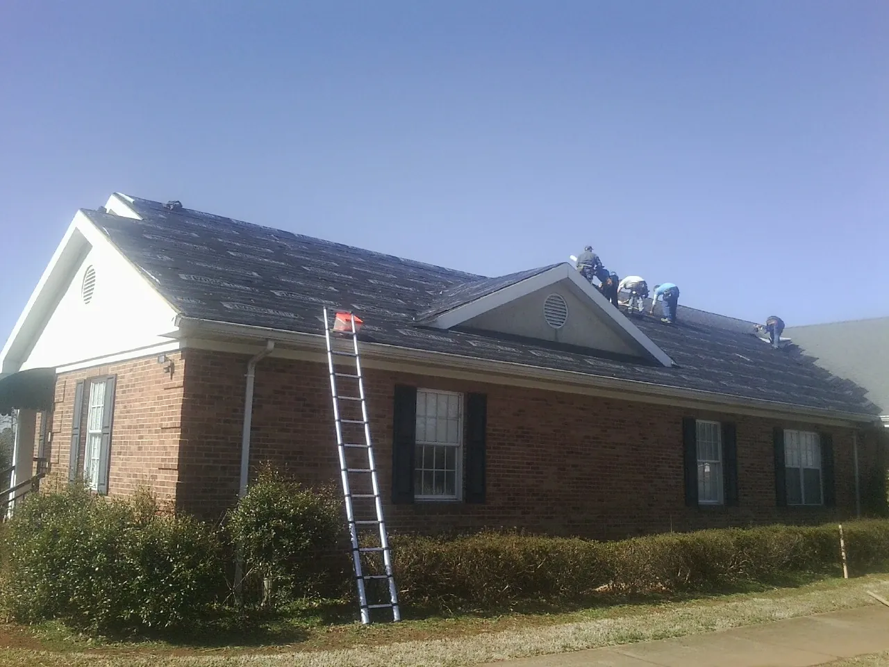 Crew tearing shingles off a brick ranch roof with a ladder set — Metal Roof Repair work by our crew in Braselton