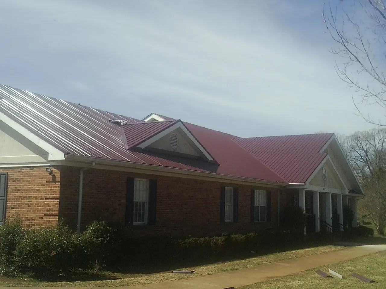 Red metal roof with gabled entries on a long brick building, from a Hail Damage Roof Repair job in Braselton