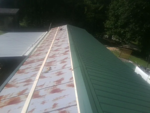 Old rusted panels beside newly installed green metal roofing — Wind Damage Roof Repair by Roofing Brothers in Braselton