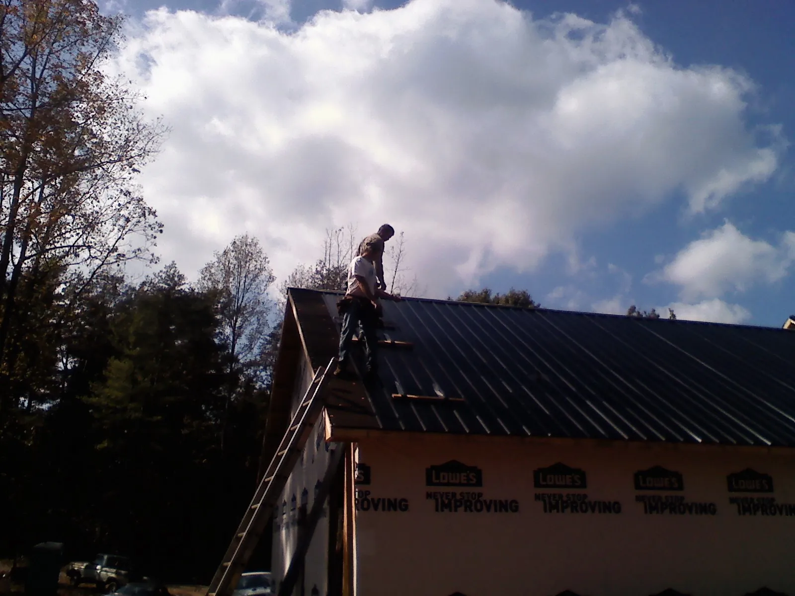 Roofer fastening dark metal panels high against a cloudy sky, from a Roof Inspection job in Braselton