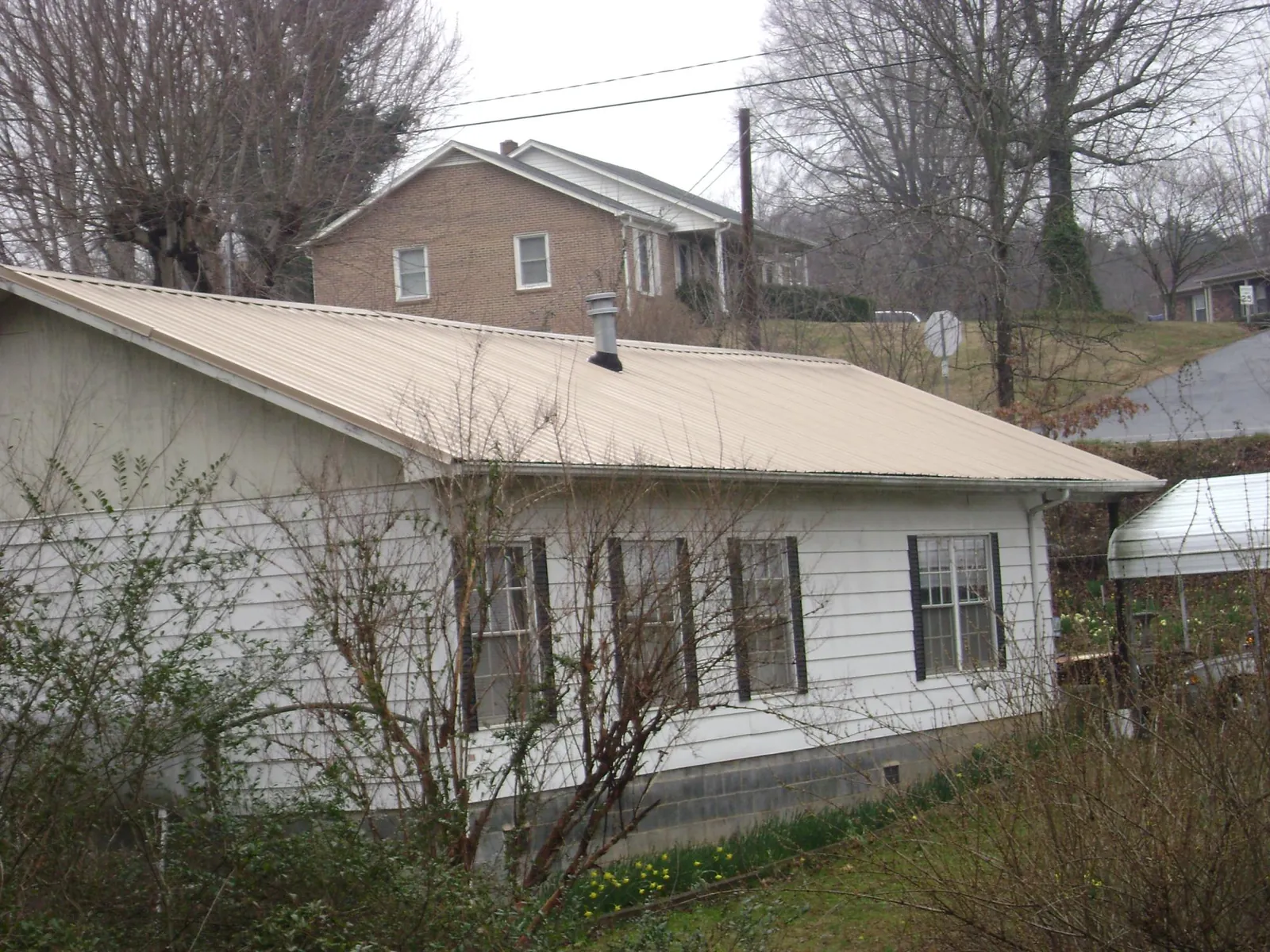 Tan metal roof on a white sided house set into a hillside — Commercial Roofing by Roofing Brothers in Braselton